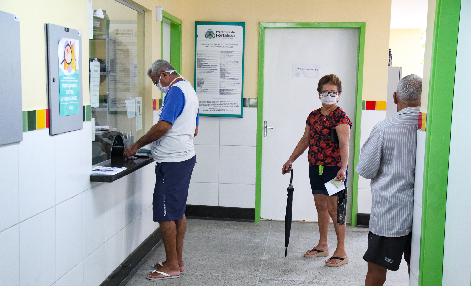 dois homens e uma mulher aguardando atendimento em recepção de posto de saúde